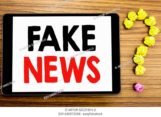 Writing text showing Fake News. Business concept for Hoax Journalism written on tablet computer on wooden background with question mark made of folded paper