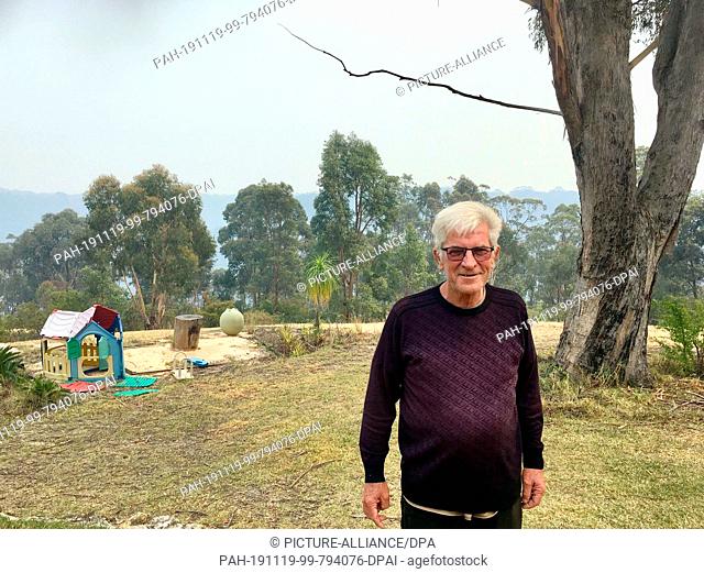 18 November 2019, Australia, Colo Heights: The 71-year-old Dave Davey is standing in the garden of his house - in the background there is smoke from the...