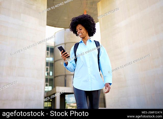 Smiling young businesswoman using smart phone amidst wall