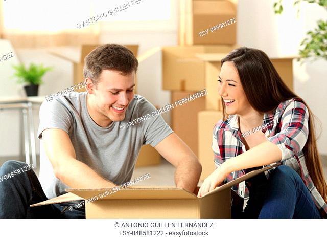 Couple moving home packing belongings in a cardboard box sitting on the floor of the living room