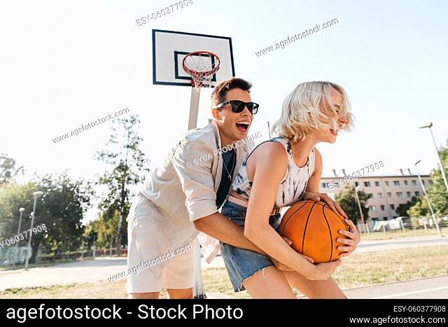 happy couple playing on basketball on playground