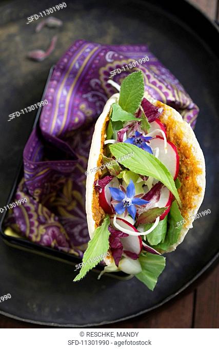 A pita bread filled with a mixed leaf salad, radishes and borage flowers