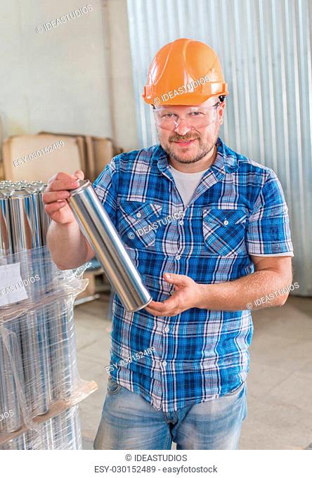 Worker smiling in safety helmet at the storage with tin blank tubes