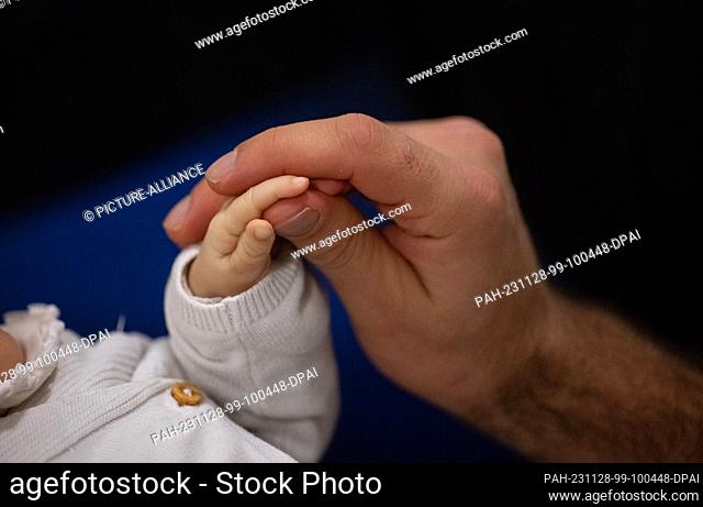 SYMBOL - 24 November 2023, Baden-Württemberg, Stuttgart: A father touches his child's hand during an infant handling course