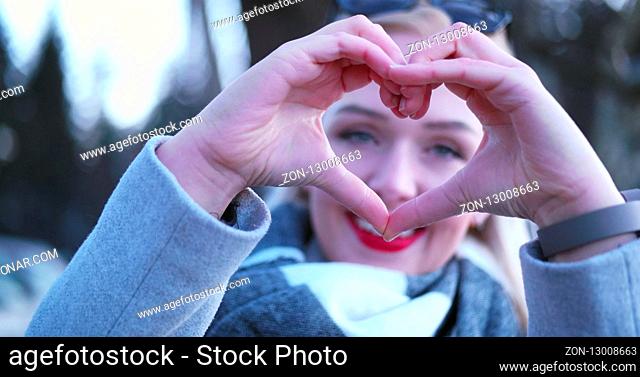 Beautiful caucasian blonde woman showing heart sign with fingers, valentine day concept love