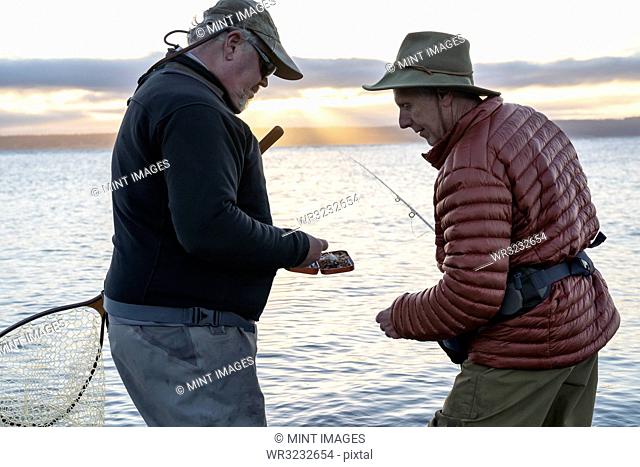 A male fly fisherman watches his guide work putting on a new fly to try for salmon or trout at a salt water beach