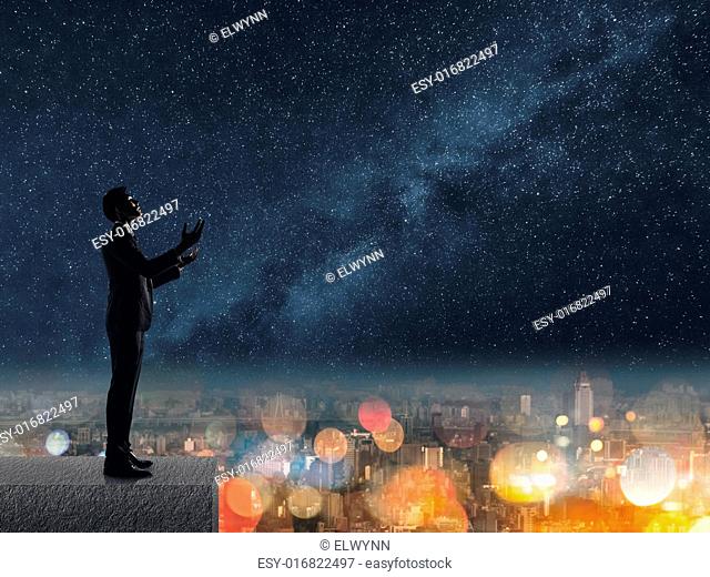 Silhouette of Asian businessman standing and praying at the roof under stars night in city