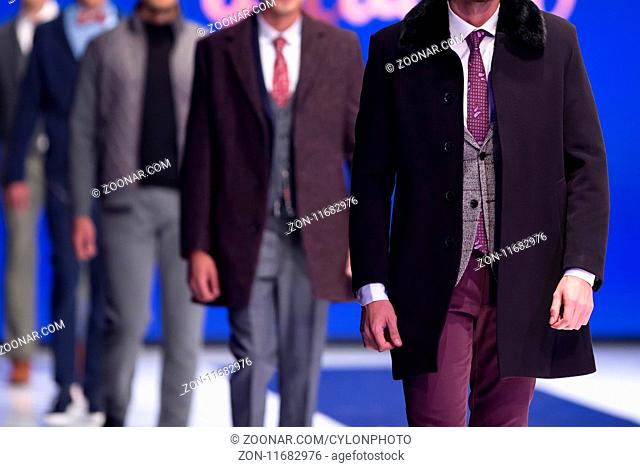 Male models walk the runway in stylish suits during a Fashion Show. Fashion catwalk event showing new collection of clothes. Single model