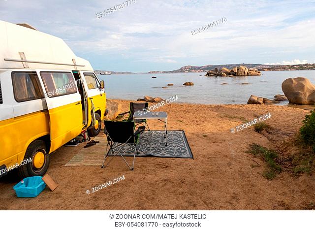 Retro minivan car on camping spot on beach near Palau, Costa Smeralda, Sardinia, Italy. Summer holidays, road trip, vacation and travel and concept