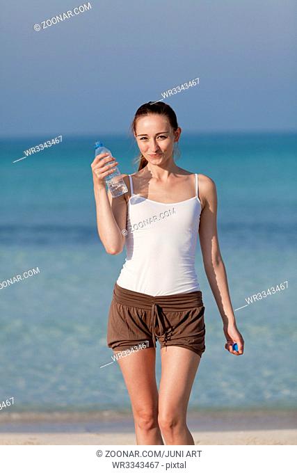 Junge Frau mädchen trinkt erfrischendes Wasser aus einer Flasche am Strand am Meer im Sommer Urlaub