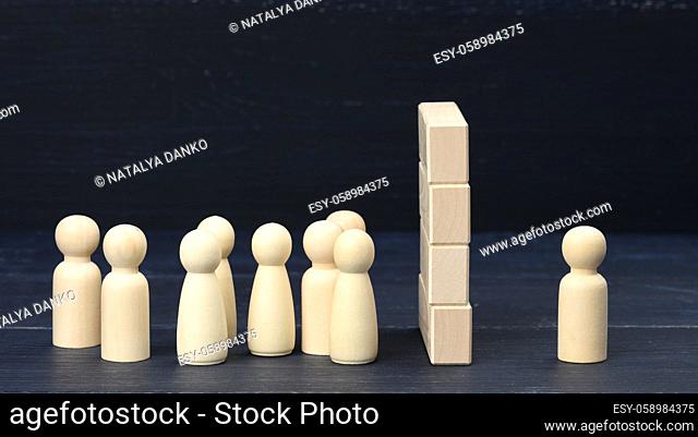 wooden figures of men the crowd stands in front of a wall of wooden blocks, on the other side one figure. The concept of a quarrel and misunderstanding