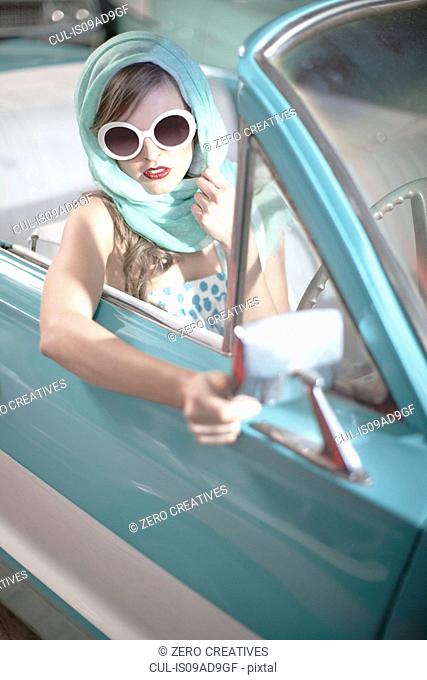 Woman in headscarf and white sunglasses in vintage convertible