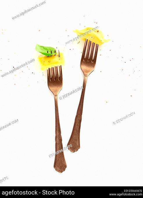 Italian pasta design. An overhead photo of two vintage forks with ravioli, basil and pepper on a white background with copy space