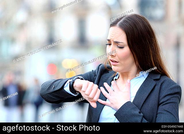 Portrait of a worried business woman holding chest checking scared her pulse on a smart watch on a city street