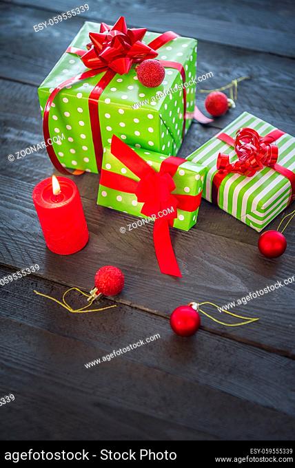 Many cheerful gifts, wrapped in green paper and tied with red ribbons and bows, surrounded by Xmas decorations, and a lit candle, on a vintage wooden table