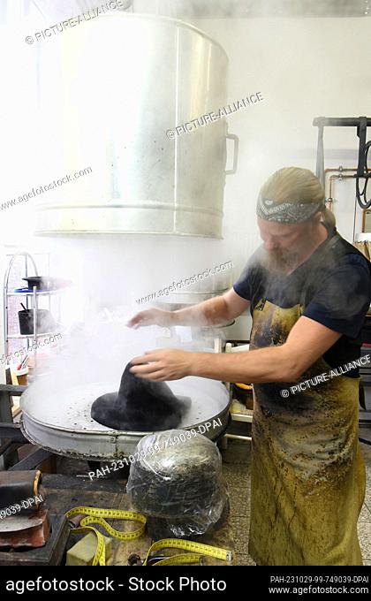 24 October 2023, Thuringia, Altenburg: At Hut und Kostüm GmbH, milliner Thomas Krause works on a blank for a Biedermeier cylinder on a steam boiler