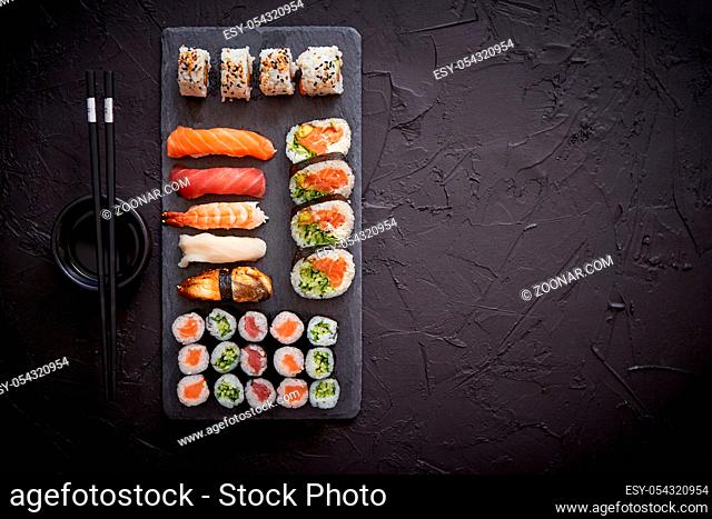 Sushi rolls set with salmon and tuna fish served on black stone board. Top view of traditional japanese cuisine. Asian food on black stone slate with chopsticks