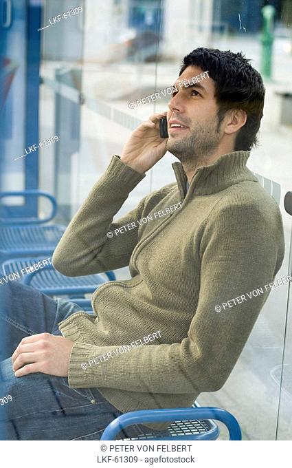 Young man at bus stop phoning with a mobile phone