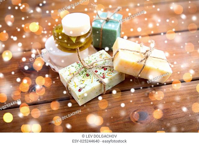 beauty, spa, bodycare, bath and natural cosmetics concept - handmade soap bars on wood over lights and snow