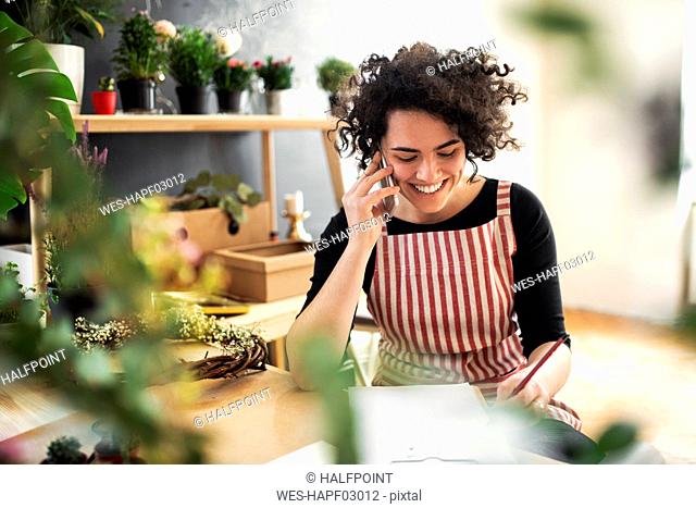 Happy young woman on the phone in a small shop with plants