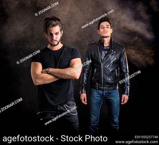 Two attractive young hard rock men posing in studio. Black background