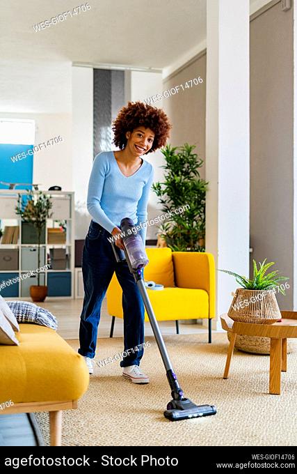 Smiling young Afro woman cleaning carpet in living room at home