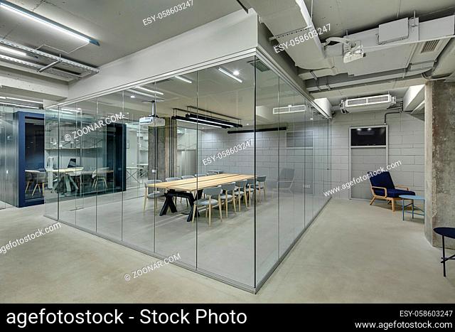 Conference zone in the office in a loft style with brick walls and concrete columns. Zone has a wooden table with gray chairs and glass walls