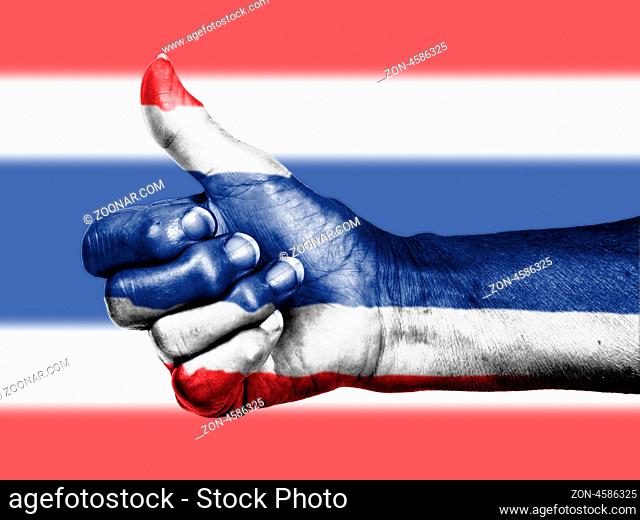 Old woman with arthritis giving the thumbs up sign, wrapped in flag pattern, Thailand
