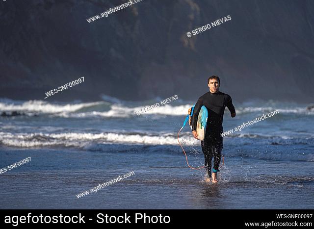Handicapped surfer with surfboard running at beach