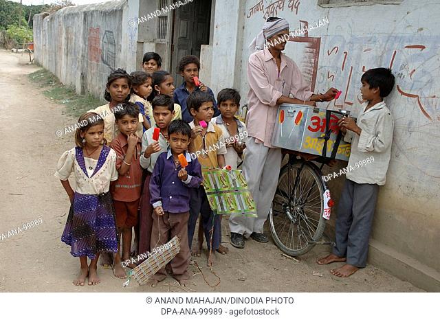 School going children eating red color ice cream , Village Manghawa , District Narsinghpur , Madhya Pradesh , India