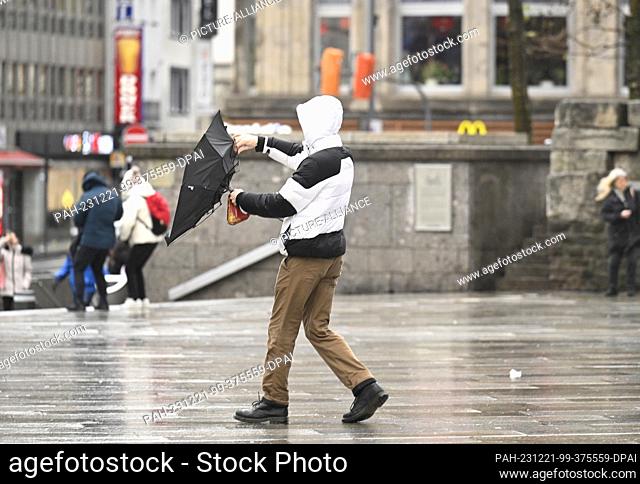 21 December 2023, North Rhine-Westphalia, Cologne: A man struggles with his umbrella in stormy weather Photo: Roberto Pfeil/dpa