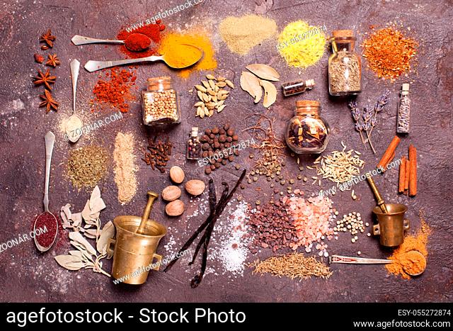 Flat lay composition of various spices and mortars over brown slate background, top view