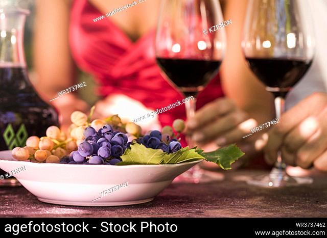 Man and woman drinking read wine and eating grapes, close up