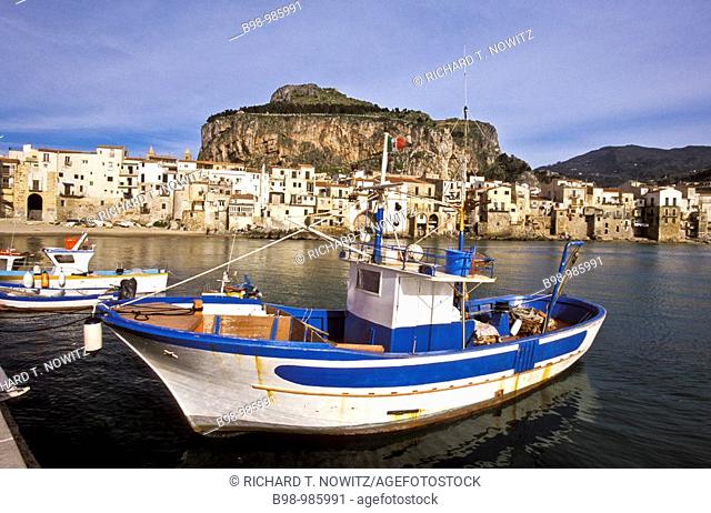 Cefalu, Sicily, Italy  Fishing harbor of the medieval town in late afternoon light  Boats tied to dock  Village and giant rock 'la rocca' in background...