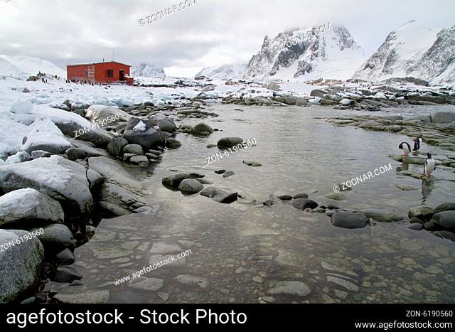 old research station and a colony of penguins around the mountains in the background of the Antarctic Peninsula