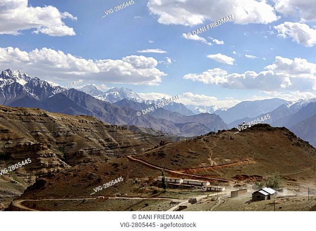 Vehicles travel down a dusty road to a remote mountain settlement surrounded by magnificent mountains a few hours away from the town of Kargil in Ladakh, India
