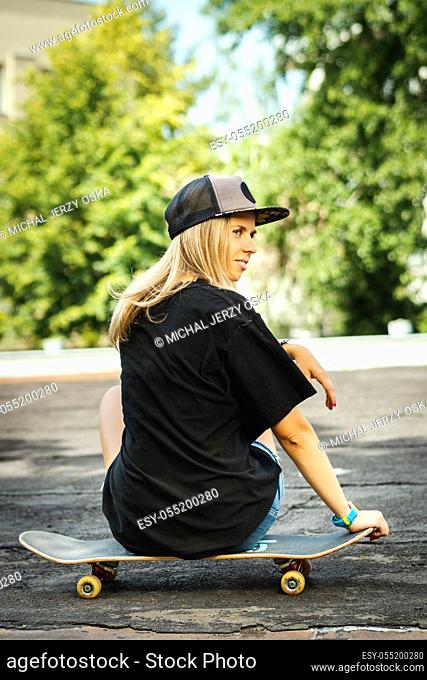 girl in a black T-shirt is sitting with her back on a skateboard and looks around