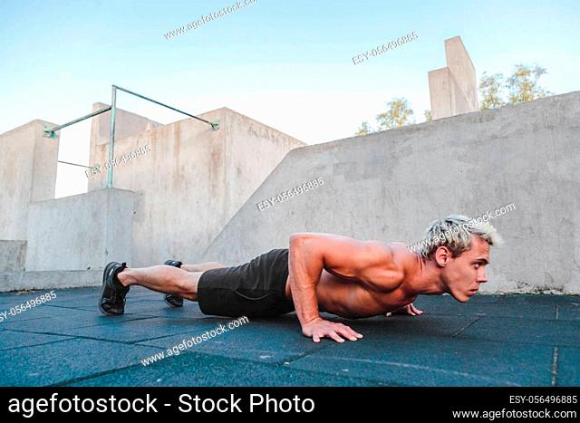 Young athletic man doing push ups on parkour area. Training alone outdoors