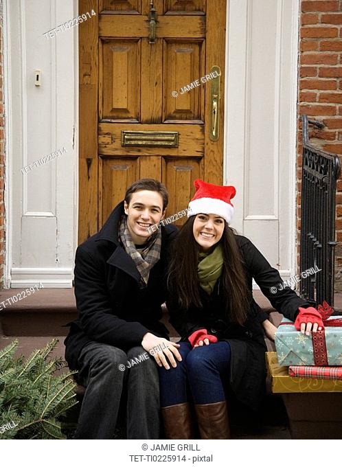 Couple with Christmas tree and gifts in front of door