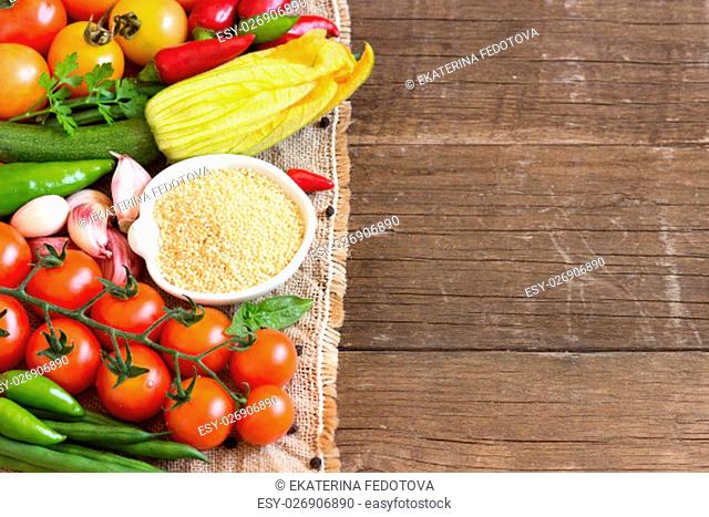 Raw Organic millet in bowl and vegetables on the wooden table