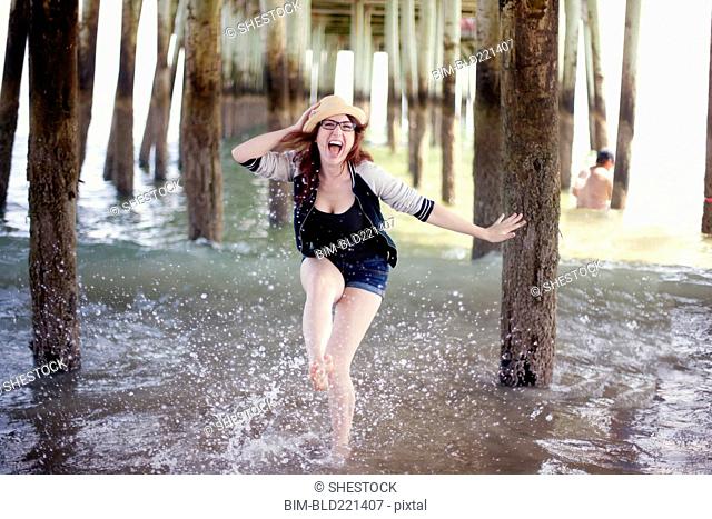 Caucasian woman splashing in ocean under boardwalk