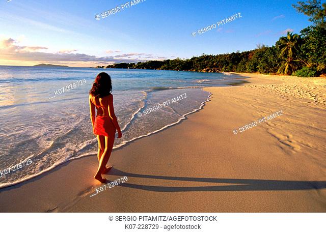 Woman walking on desert beach at sunset. Praslin Island. Seychelles