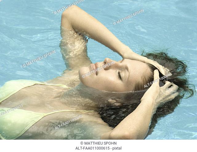Woman in pool, head back and hands in hair with eyes closed