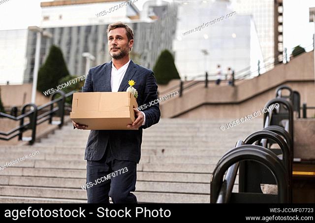 Worried businessman with cardboard box moving down stairs