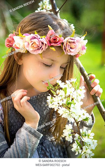 Little girl with wreath of flowers smelling blossoming branch