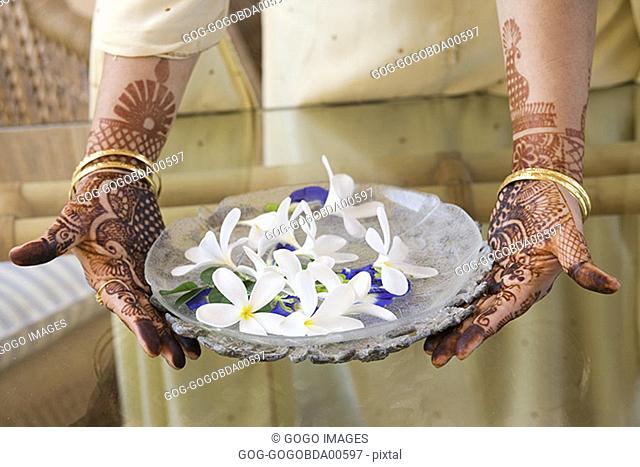 Woman with tattooed hands carrying a bowl of flowers