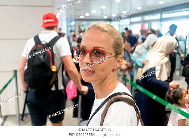 Young blond caucasian woman waiting in long line at security check at the departure airport terminal. Lady standing in long queue at airport before boarding a...