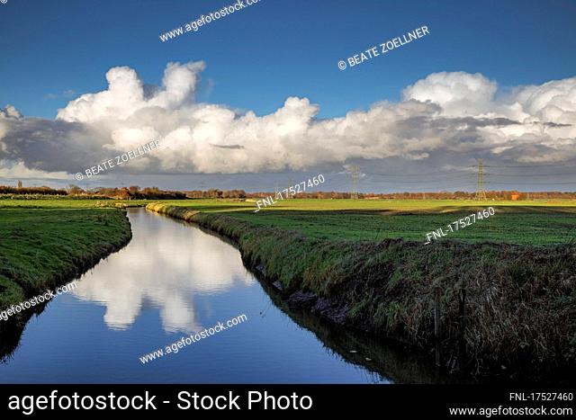 Band of clouds illuminated by autumn sun reflected on a moat crossing the marshland