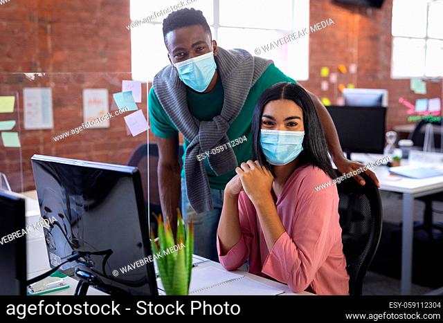 Portrait of diverse business colleagues wearing face masks brainstorming in front of computer