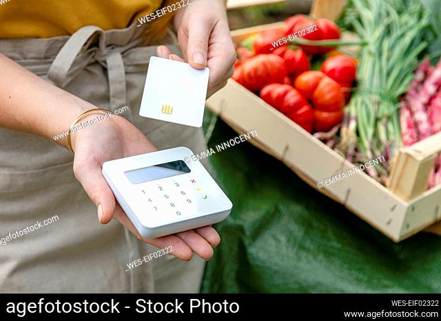 Female farmer with credit card holding wireless card reader by vegetable's crate